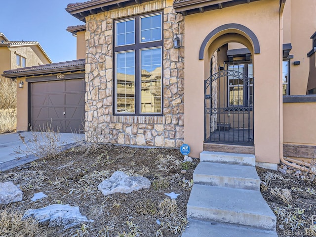 doorway to property with a garage, stone siding, a gate, and stucco siding