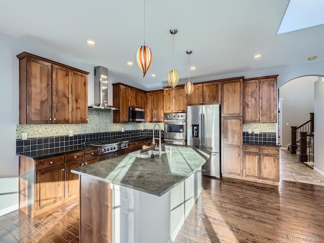 2256 S Isabell Ct, Lakewood, CO 80228 - kitchen featuring wall chimney range hood, stainless steel appliances, a sink, arched walkways, and hardwood / wood-style flooring