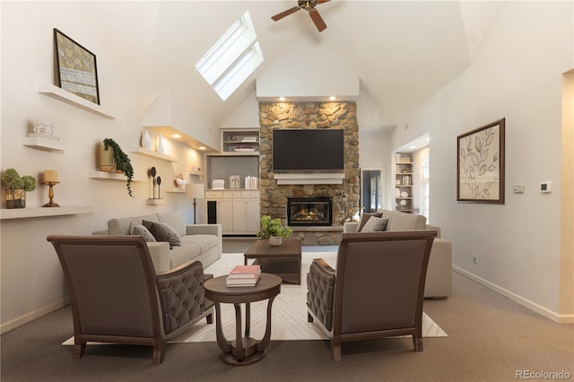 carpeted living room with a skylight, ceiling fan, a stone fireplace, built in features, and high vaulted ceiling