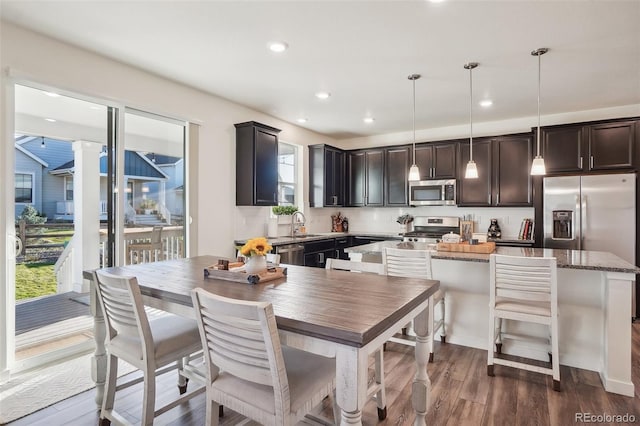 kitchen featuring light stone countertops, appliances with stainless steel finishes, a center island, dark hardwood / wood-style floors, and hanging light fixtures