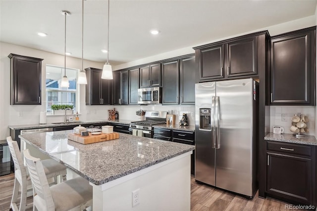 kitchen with a breakfast bar, sink, appliances with stainless steel finishes, decorative light fixtures, and a kitchen island