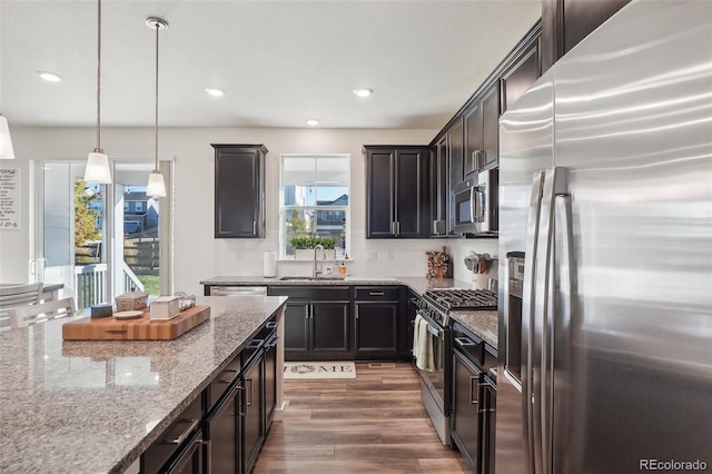 kitchen with light stone countertops, appliances with stainless steel finishes, dark hardwood / wood-style flooring, sink, and decorative light fixtures