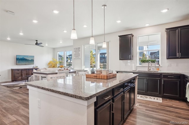 kitchen with ceiling fan, sink, hanging light fixtures, wood-type flooring, and a kitchen island