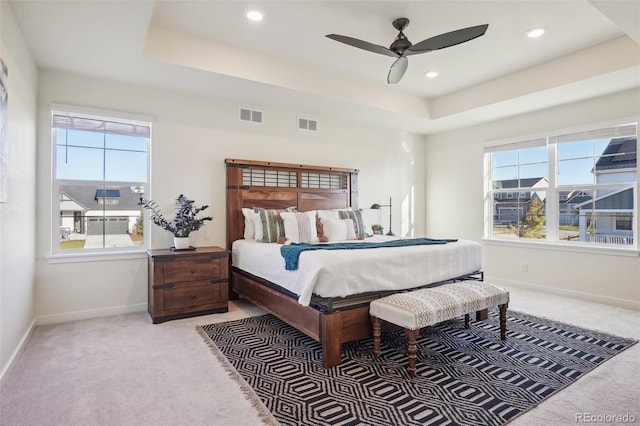 bedroom with light colored carpet, a raised ceiling, and ceiling fan