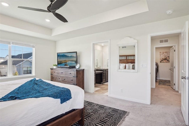 carpeted bedroom with a raised ceiling, connected bathroom, and ceiling fan