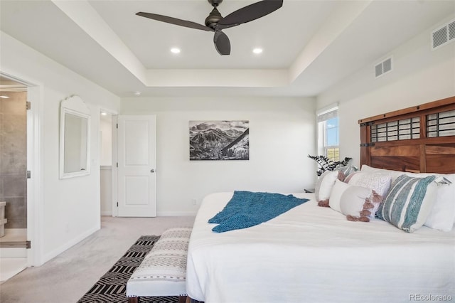 carpeted bedroom with a raised ceiling, ensuite bath, and ceiling fan