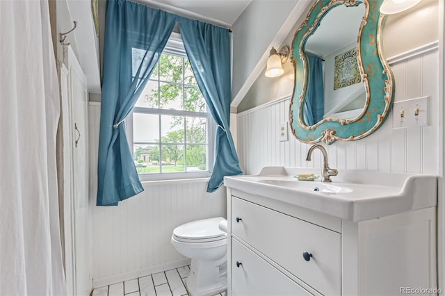 134 S 5th Ave, Brighton, CO 80601 - bathroom featuring vanity, toilet, wainscoting, and a decorative wall