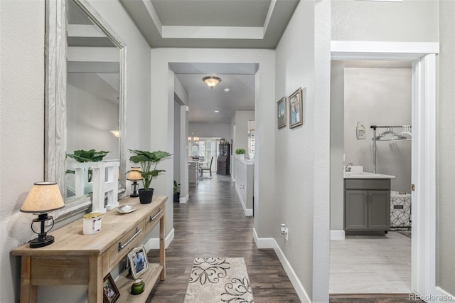 hall with a raised ceiling, an inviting chandelier, dark wood finished floors, and baseboards