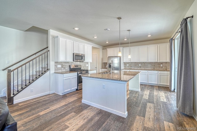 kitchen with stainless steel appliances, an island with sink, hanging light fixtures, and white cabinets