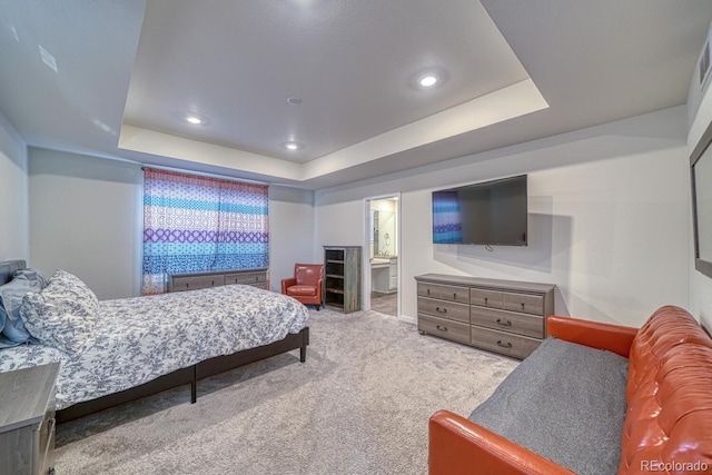 bedroom with ensuite bath, a raised ceiling, and light carpet