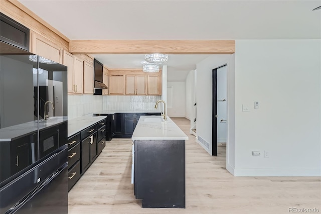 kitchen featuring sink, backsplash, a kitchen island with sink, light brown cabinets, and light hardwood / wood-style flooring