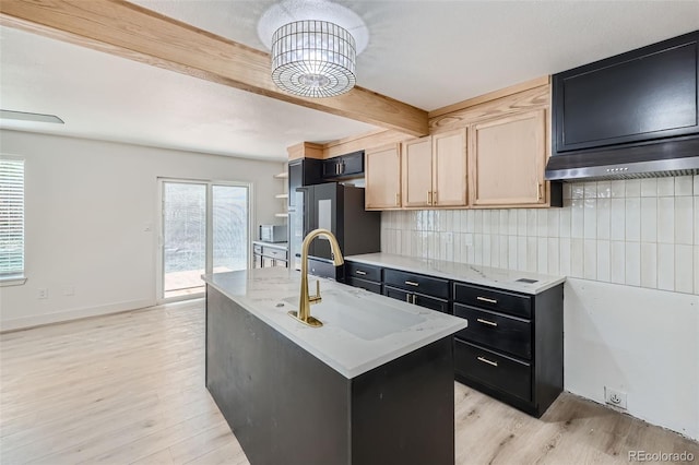 kitchen featuring sink, stainless steel refrigerator, an island with sink, decorative backsplash, and light wood-type flooring