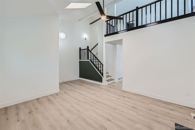 unfurnished living room with ceiling fan, high vaulted ceiling, a skylight, and light hardwood / wood-style floors