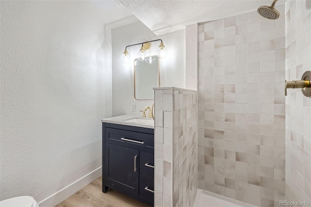 bathroom with hardwood / wood-style flooring, vanity, a textured ceiling, and a tile shower