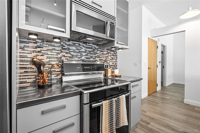 3100 Huron St Unit 1A, Denver, CO 80202 - kitchen featuring stainless steel appliances, stainless steel countertops, decorative backsplash, light wood-style floors, and glass insert cabinets