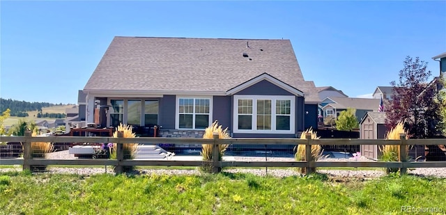 rear view of property featuring a shingled roof, fence, and an outdoor structure