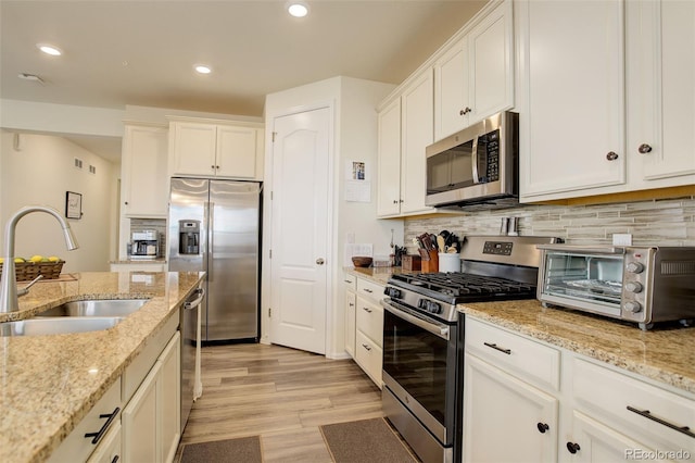 kitchen featuring a toaster, decorative backsplash, appliances with stainless steel finishes, white cabinetry, and a sink