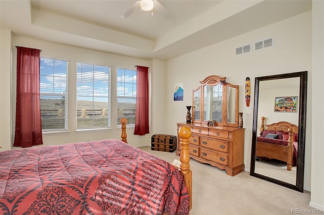 bedroom with ceiling fan, a raised ceiling, visible vents, and light colored carpet