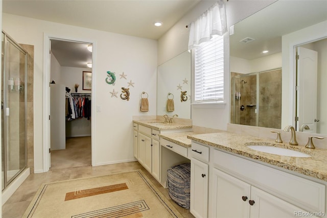 full bath featuring a stall shower, two vanities, a sink, and a walk in closet