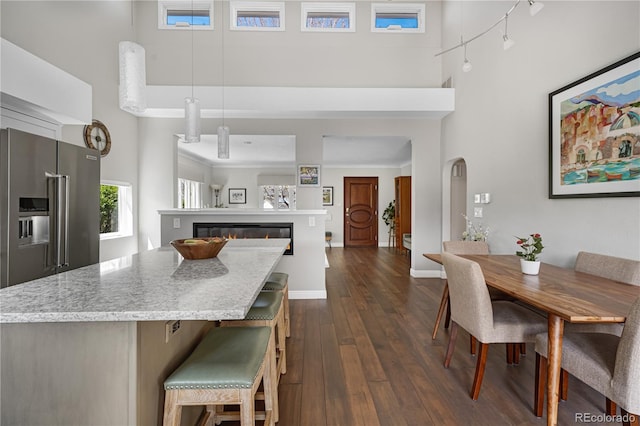 dining room with a towering ceiling, dark wood-type flooring, a glass covered fireplace, and baseboards