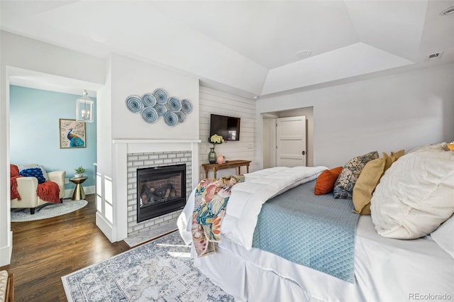 bedroom featuring lofted ceiling, dark wood-type flooring, a fireplace, and a tray ceiling