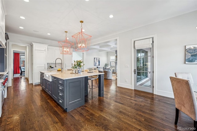 kitchen featuring a kitchen bar, sink, a center island with sink, pendant lighting, and white cabinets