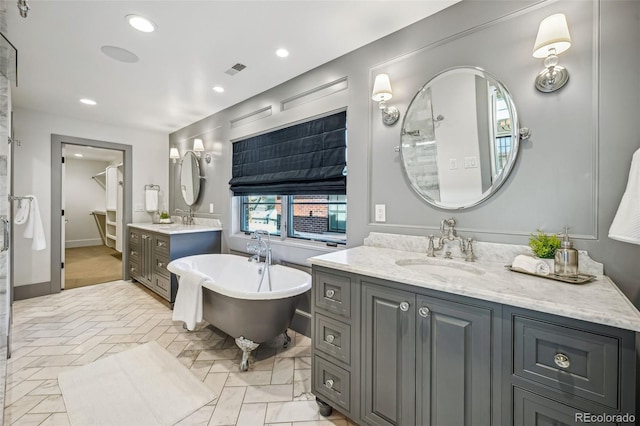 full bath with a freestanding bath, recessed lighting, a sink, and two vanities