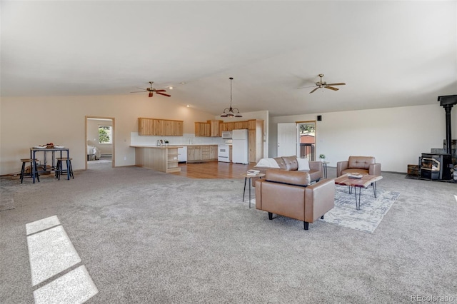 living room featuring light carpet, vaulted ceiling, a wood stove, and ceiling fan