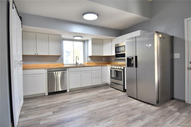 kitchen with wood counters, sink, appliances with stainless steel finishes, light hardwood / wood-style floors, and white cabinetry