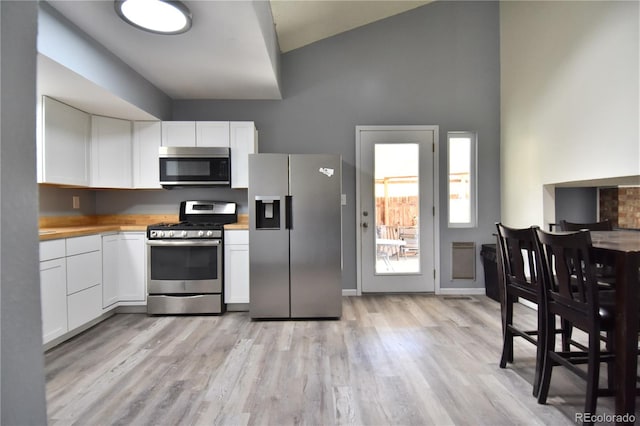 kitchen featuring white cabinets, light wood-type flooring, appliances with stainless steel finishes, and a towering ceiling