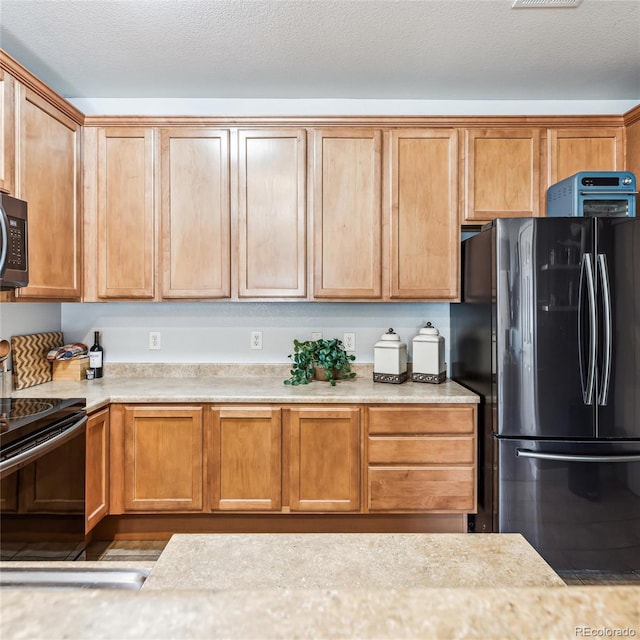 kitchen with black electric range oven, stainless steel refrigerator, and a textured ceiling