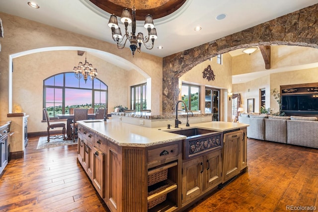 kitchen with an island with sink, sink, dark wood-type flooring, and an inviting chandelier