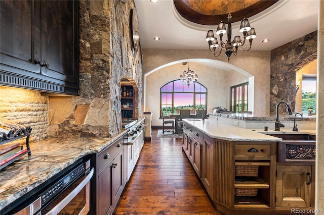 kitchen with dark hardwood / wood-style floors, light stone countertops, a tray ceiling, pendant lighting, and an inviting chandelier