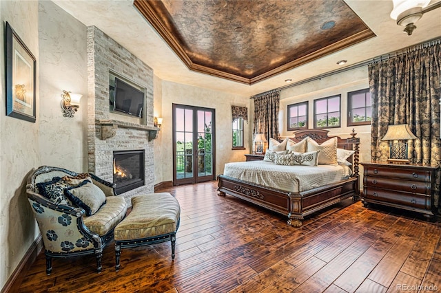 bedroom with a tray ceiling, hardwood / wood-style flooring, a fireplace, and multiple windows