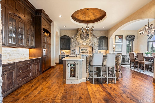 kitchen with a chandelier, dark hardwood / wood-style floors, a center island with sink, and a raised ceiling