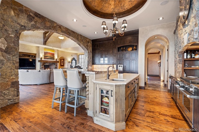 kitchen featuring range with two ovens, a raised ceiling, a kitchen island with sink, wood-type flooring, and sink