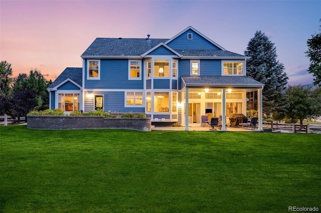 back of house at dusk with a yard, a patio, and a shingled roof