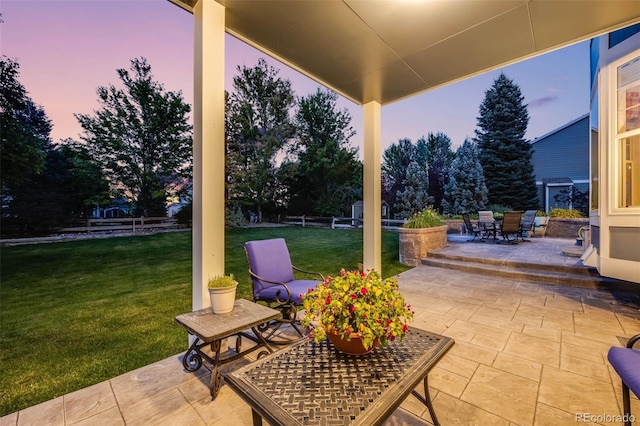 patio terrace at dusk with outdoor dining area, a yard, and fence