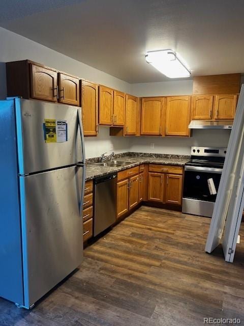 kitchen featuring under cabinet range hood, a sink, dark wood-style floors, stainless steel appliances, and brown cabinetry