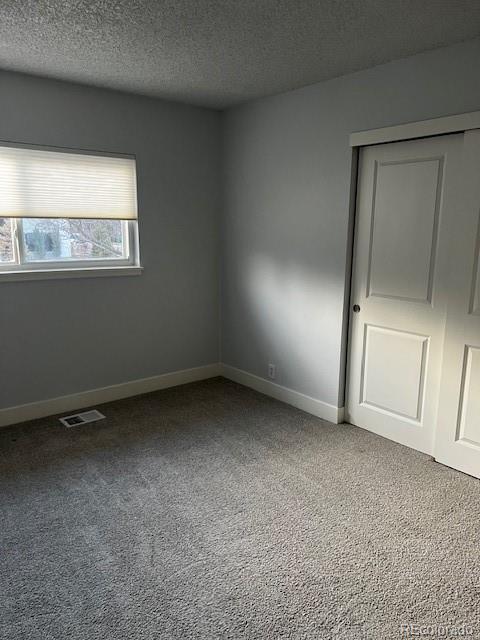 carpeted spare room with baseboards, visible vents, and a textured ceiling