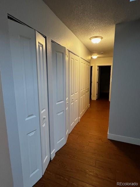 corridor with baseboards, dark wood-style flooring, and a textured ceiling