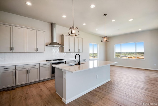 kitchen featuring wall chimney range hood, stainless steel appliances, sink, and an island with sink