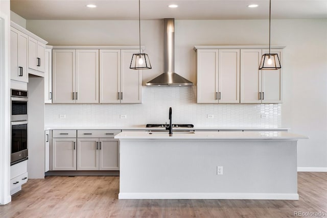 kitchen with gas stovetop, light hardwood / wood-style flooring, hanging light fixtures, a kitchen island with sink, and wall chimney range hood