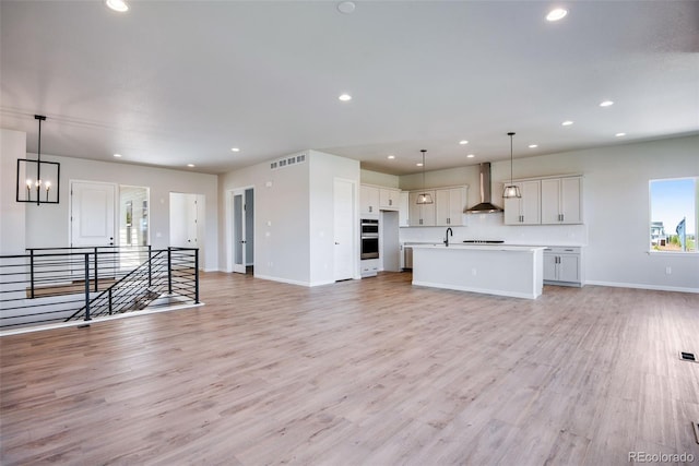 unfurnished living room featuring sink, a notable chandelier, and light hardwood / wood-style floors