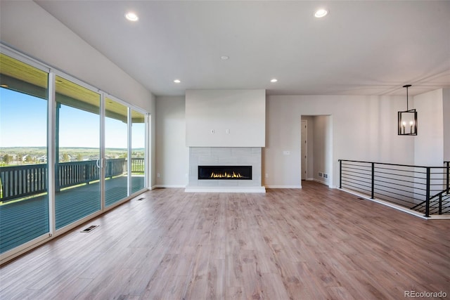 unfurnished living room featuring an inviting chandelier, light hardwood / wood-style floors, and a tile fireplace