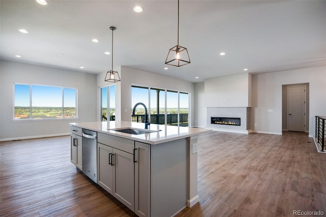 kitchen featuring sink, gray cabinetry, hanging light fixtures, an island with sink, and light wood-type flooring