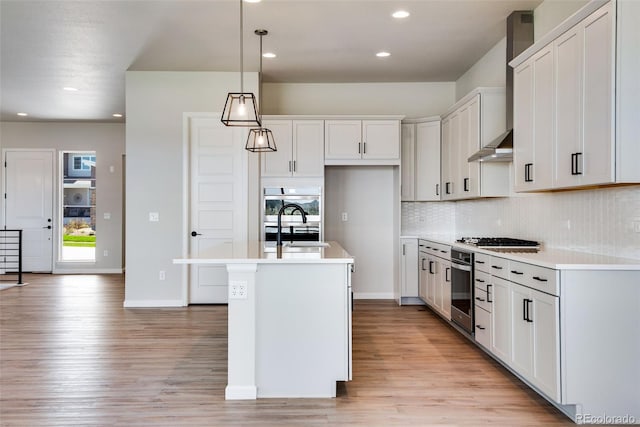 kitchen featuring appliances with stainless steel finishes, decorative light fixtures, white cabinetry, sink, and a kitchen island with sink