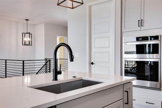 kitchen featuring double oven, decorative light fixtures, light stone countertops, and sink