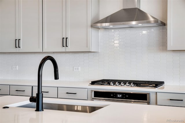 kitchen with appliances with stainless steel finishes, tasteful backsplash, sink, white cabinets, and wall chimney range hood