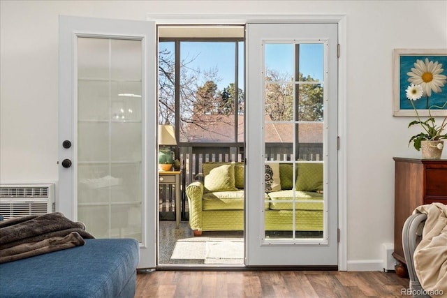 doorway to outside featuring baseboards, wood finished floors, and a wall unit AC